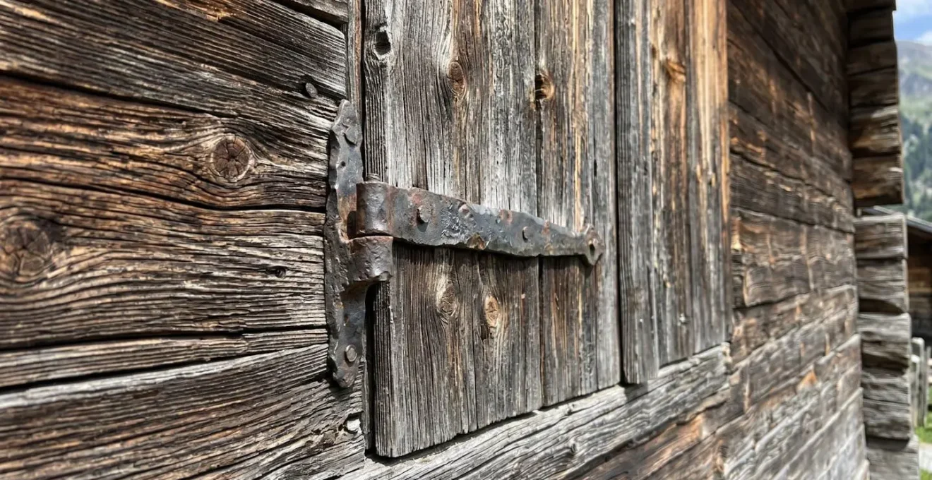 Gros plan sur la texture du bois ancien d'un chalet savoyard traditionnel avec ferronnerie ancienne visible sous une lumière naturelle rasante