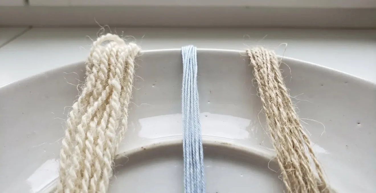 Gros plan rapproché sur trois échantillons de fils naturels côte à côte montrant la texture distincte de la laine, du coton et du lin