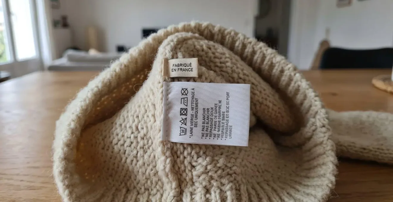 Gros plan sur étiquette de composition textile et étiquette Made in France cousues sur l'intérieur d'un pull en maille écru