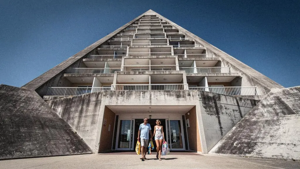 Immeuble pyramidal emblématique de La Grande-Motte vu en contre-plongée avec un couple de vacanciers en sortant