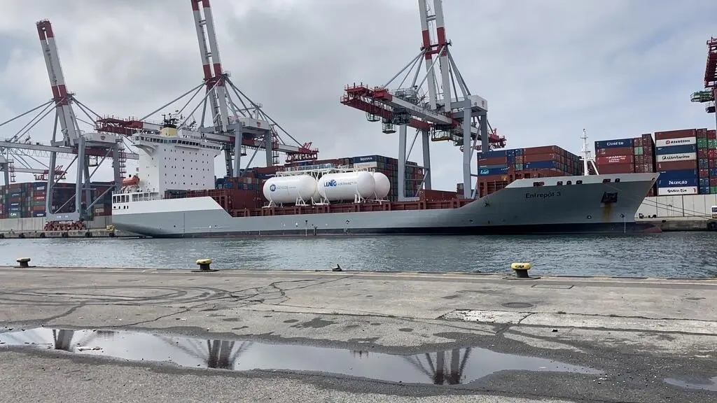 Navire cargo moderne équipé de systèmes de propulsion alternative amarré dans un port industriel français, avec infrastructures portuaires et grues de chargement en arrière-plan